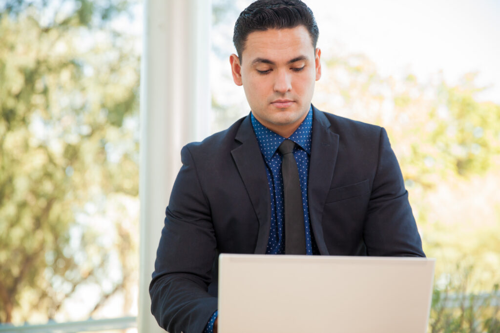 A young individual in a suit, working on his laptop in a more relaxed office setting.